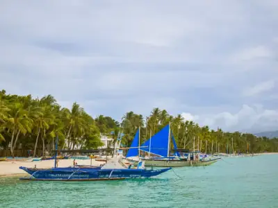 Serene tropical beach with blue sailboats and coconut trees in Boracay, Philippines.