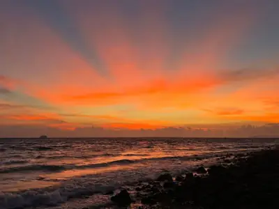 Stunning sunset over the rocky shoreline of Batangas, Philippines, showcasing vivid orange and pink skies.