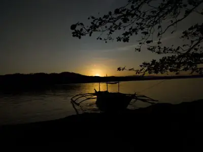 A tranquil sunset over water with a silhouetted boat in Camarines Norte, Philippines.