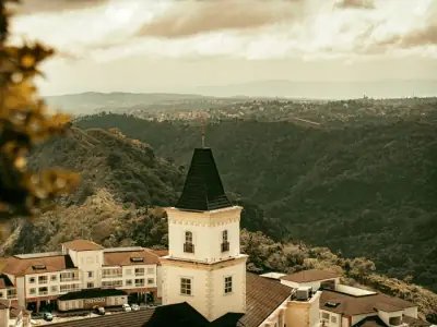 From above of aged residential houses with red roofs located in mountainous valley covered with lush green trees against cloudy sky in Tagay