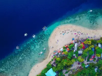 A stunning aerial view of Oslob Beach, Cebu, with vibrant blue waters and lush greenery.