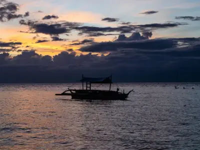 Serene sunset view with a silhouette of a traditional boat on the waters of Moalboal, Philippines.