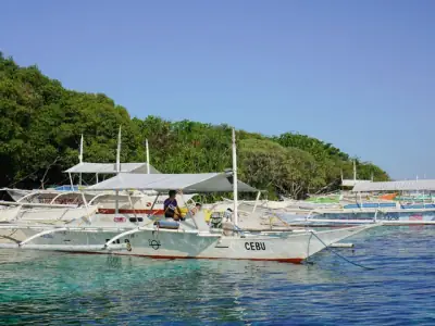 Scenic view of traditional Philippine boats moored in turquoise waters near lush green coastline of Cebu.