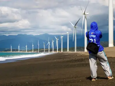 A person photographing the iconic wind turbines at Bangui Wind Farm along the beach in the Ilocos Region, Philippines.