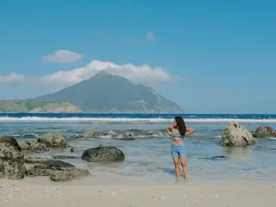 Woman enjoying a sunny day by the rocky shore in Cagayan Valley, with a distant mountain view.
