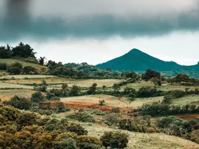 Serene countryside view of Nasugbu with rolling hills and a mountain backdrop enveloped by clouds.