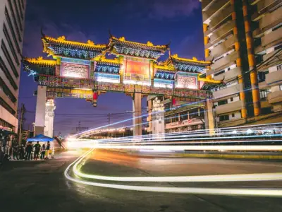 A vibrant night scene capturing the illuminated Chinese gate in Manila, showcasing cultural architecture and city life.