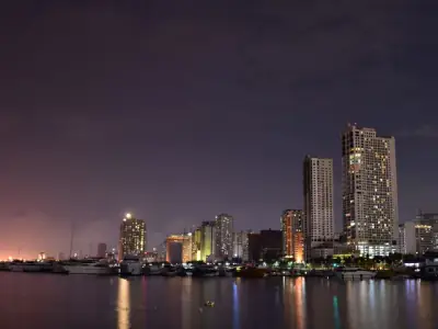 Picturesque scenery of contemporary skyscrapers located on shore of sea with moored boats against dark sundown sky in Manila