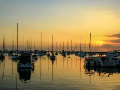 A serene view of sailboats docked at Manila Harbor during a stunning sunset, reflecting on the water.