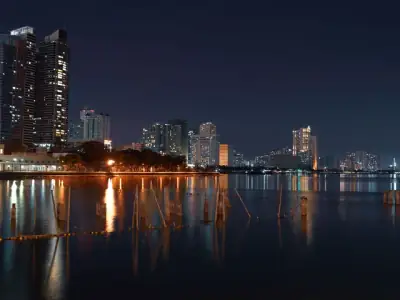 Illuminated skyscrapers reflected on the waterfront in Manila cityscape at night.
