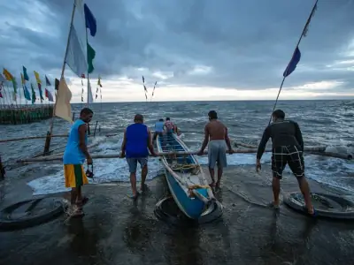 Group of fishermen launching a boat at Dumaguete seashore under a cloudy sky.