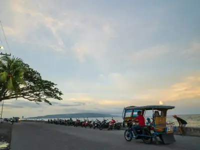 Tricycle and parked motorcycles by the sea at sunset