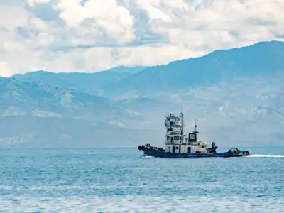 Tugboat navigating Sarangani Bay with expansive mountain backdrop under bright skies.