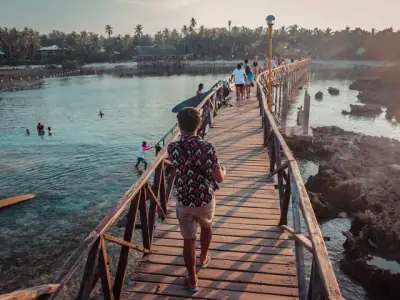 People walk across a scenic wooden bridge in General Luna, Philippines at sunset.